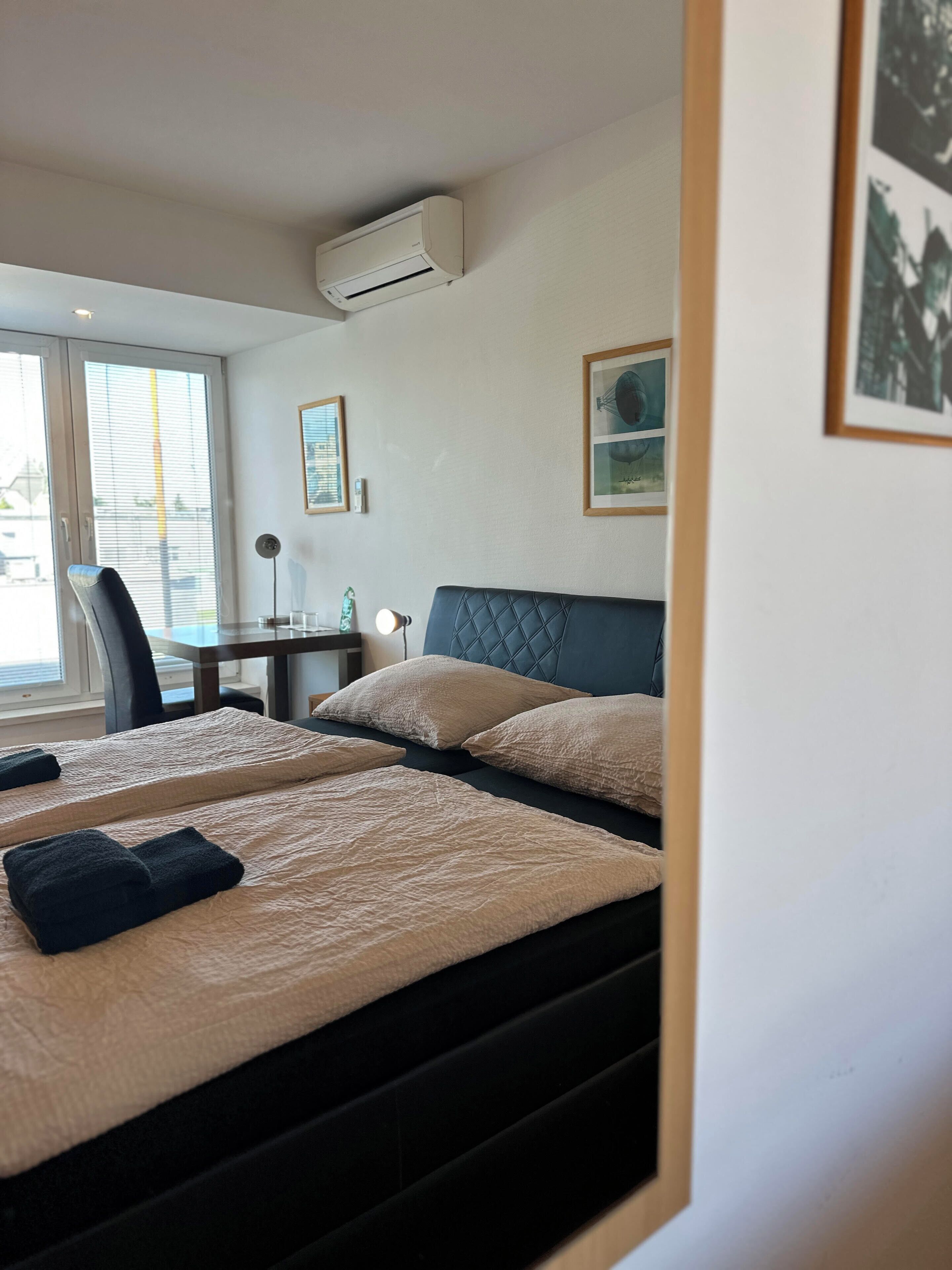 Habitación de hotel con dos camas, un escritorio y una silla. Se observa un equipo de aire acondicionado en la pared.