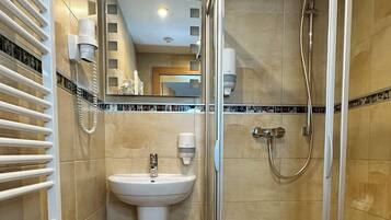 Un baño moderno con ducha envuelta en vidrio, un lavamanos y un perchero para toallas.
