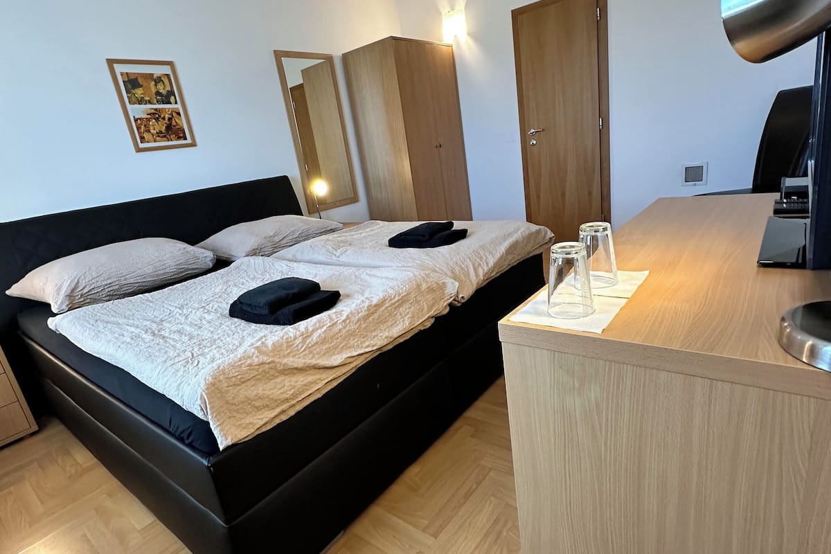 A modern hotel room with a large bed, a desk with a lamp, and a mirror.