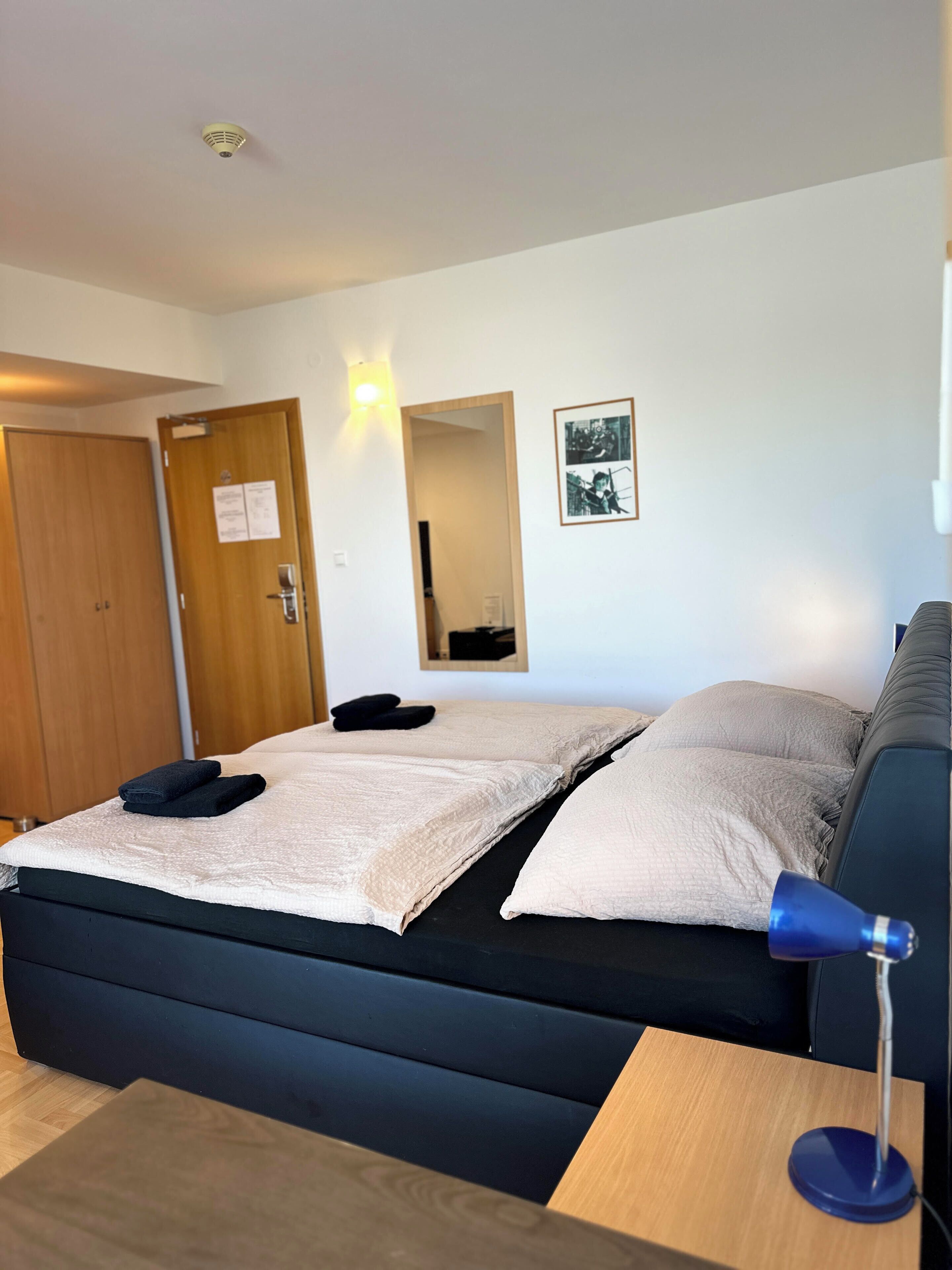A neatly made bed with a blue headboard, a bedside table with a lamp, and a wooden door with a sign.