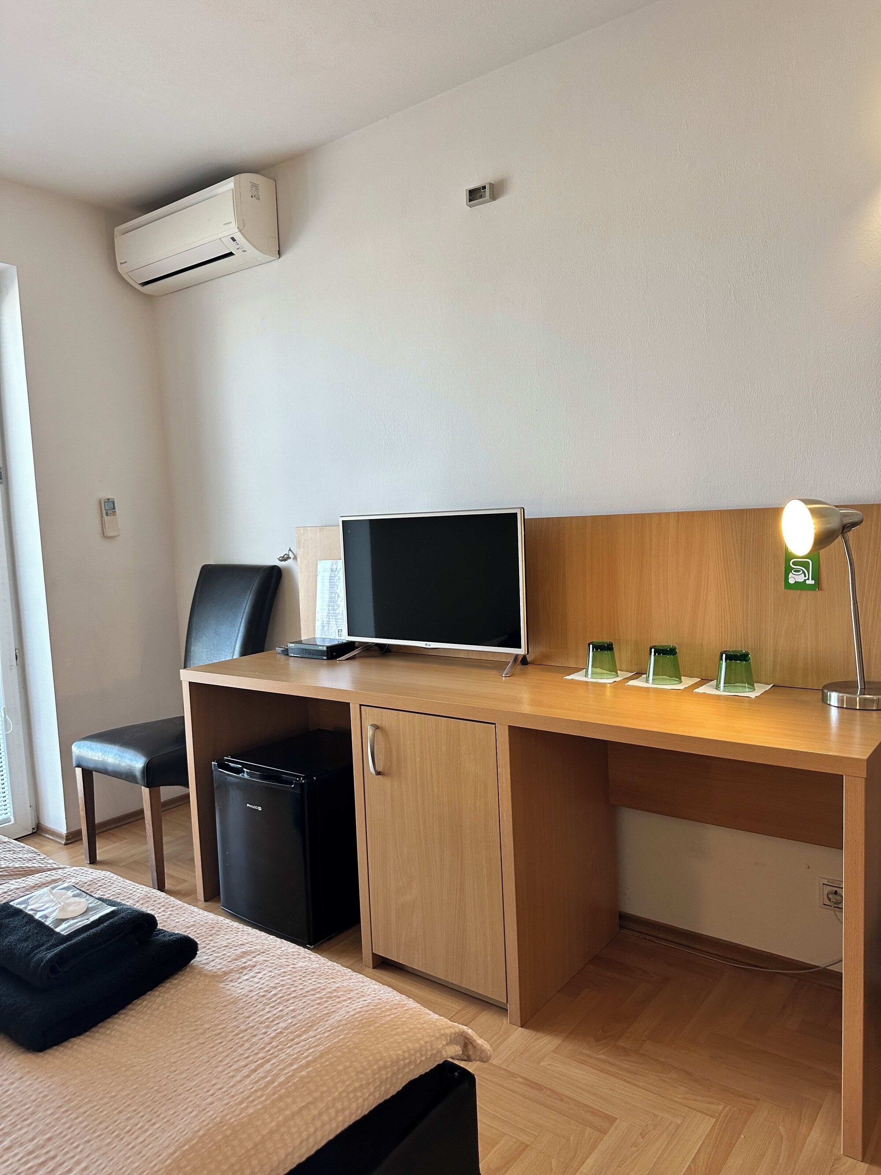 Une chambre d’hôtel comprenant un lit, un bureau avec un ordinateur, une chaise, une petite poubelle et une lampe.