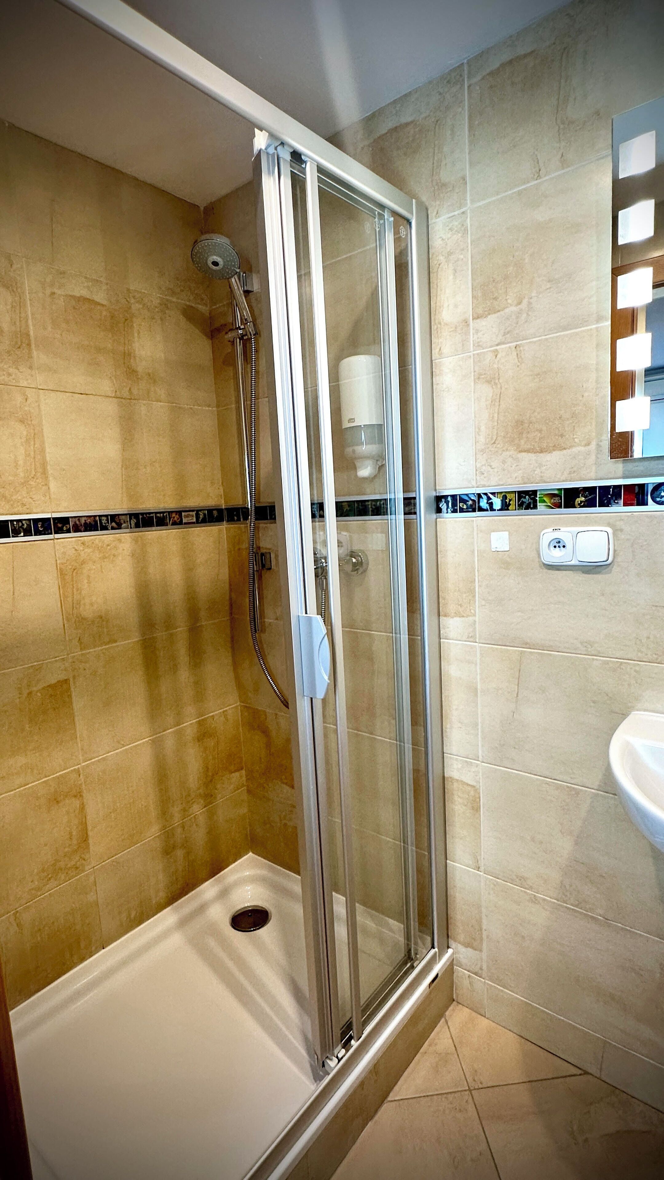 Ein modernes Badezimmer mit einer Glaskabine zur Dusche, beigen Fliesen, einem weißen Waschbecken und einem gefliesten Duschbereich.