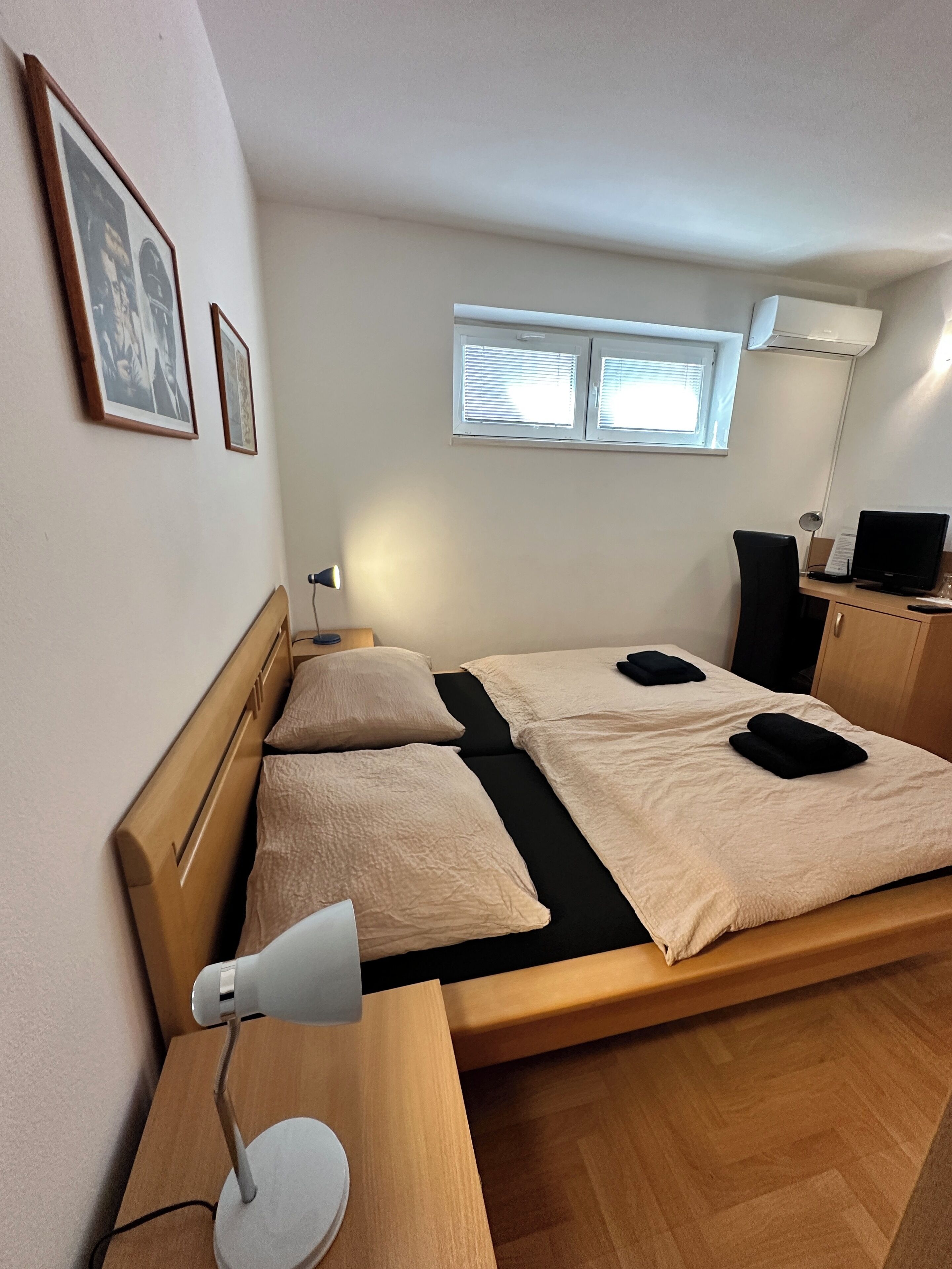 A neatly arranged bedroom with a bed, bedside table, lamp, and a desk with a chair.