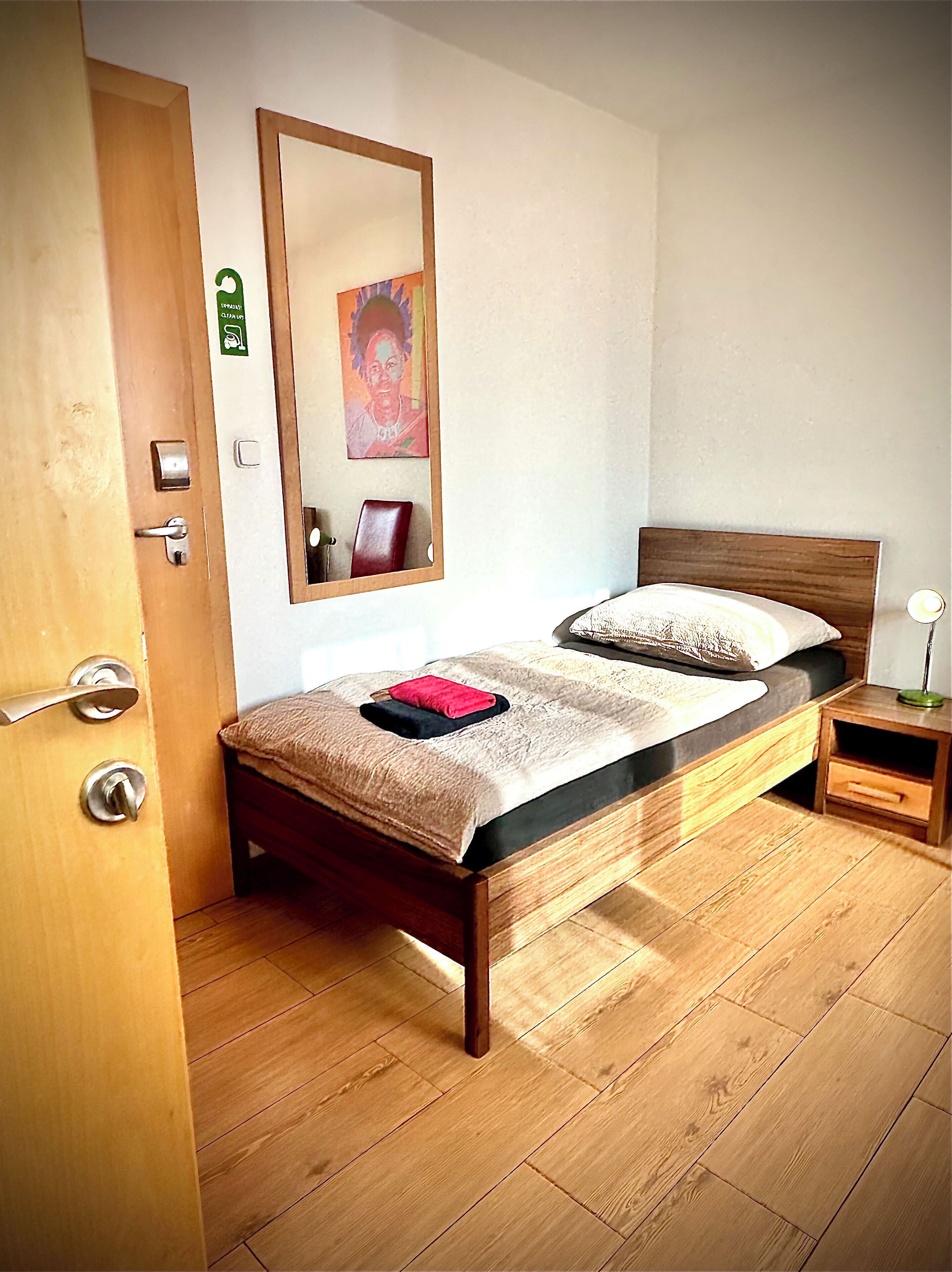 A bedroom with a wooden bed, a nightstand, a mirror, and a door.