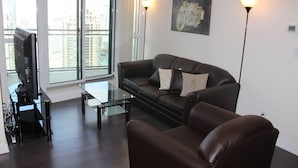 A modern living room with a leather sofa, a glass coffee table, and a flat-screen TV on a stand.