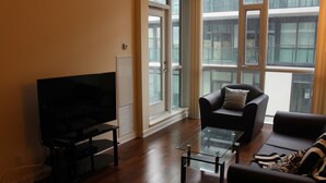A living room with a flat-screen TV, a glass coffee table, a sofa, and a chair.