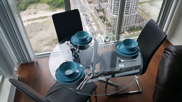 A dining table with a glass top and four blue plates, set with cutlery, in a room with a view of a cityscape.