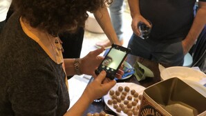 A person using a smartphone at a table with a box of biscuits and plates of round biscuits.