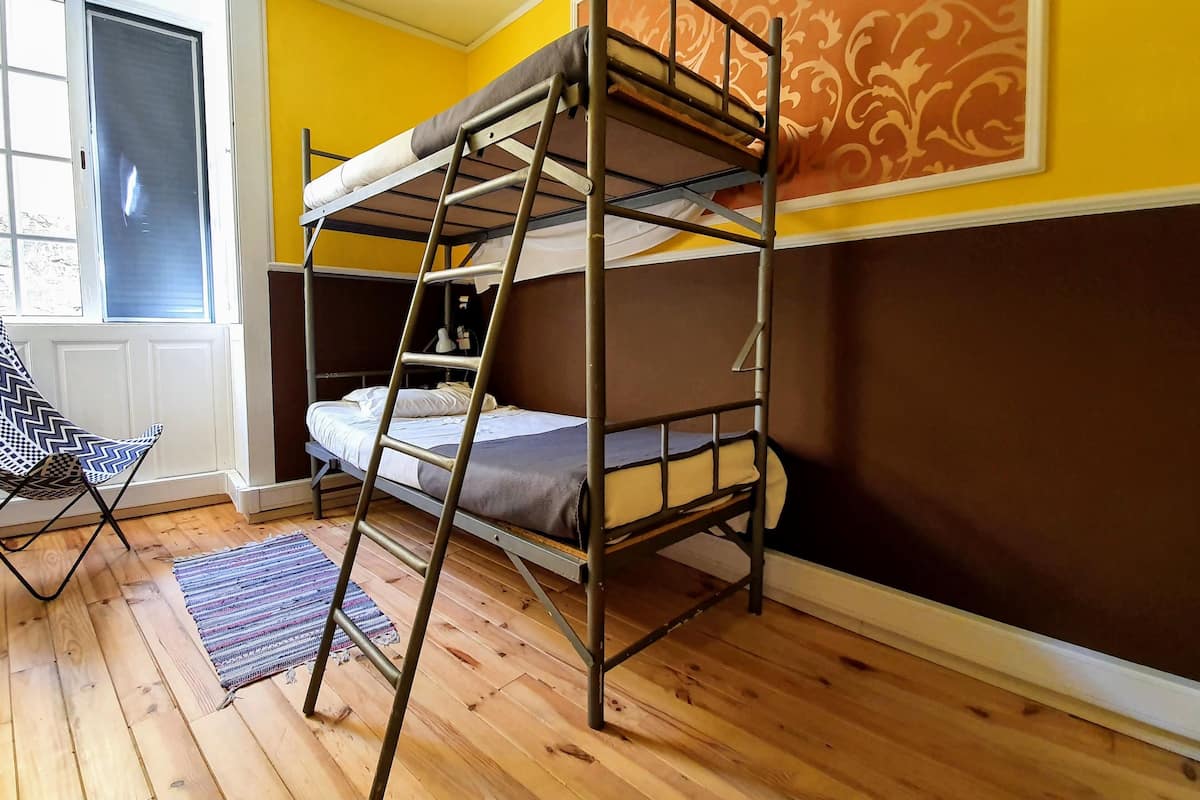 A bunk bed with a ladder, a chair, and a window with blinds.
