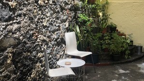 A seating area with two white chairs and a small round table, surrounded by various potted plants and a rocky wall.
