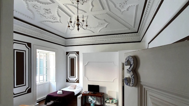A hotel room with two beds, a desk with a computer, a chair, and a decorative ceiling.
