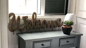 A grey console table with two drawers, a 'Welcome' sign, and a potted plant.