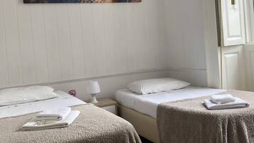 Une chambre d’hôtel avec deux lits, une table de chevet avec une lampe et un tableau représentant une scène de plage au mur.