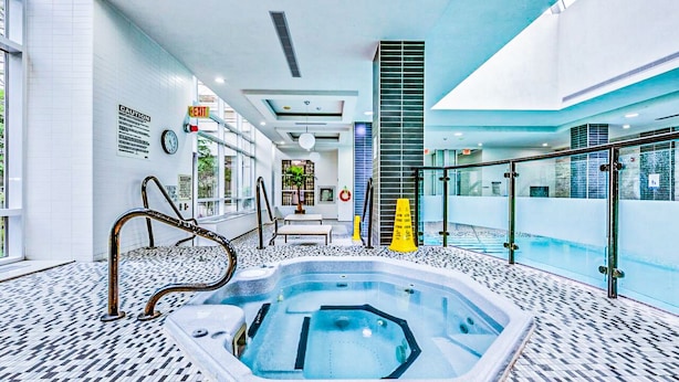 Piscina interior moderna com balaustrada de vidro, hidromassagem e piso revestido de azulejos.