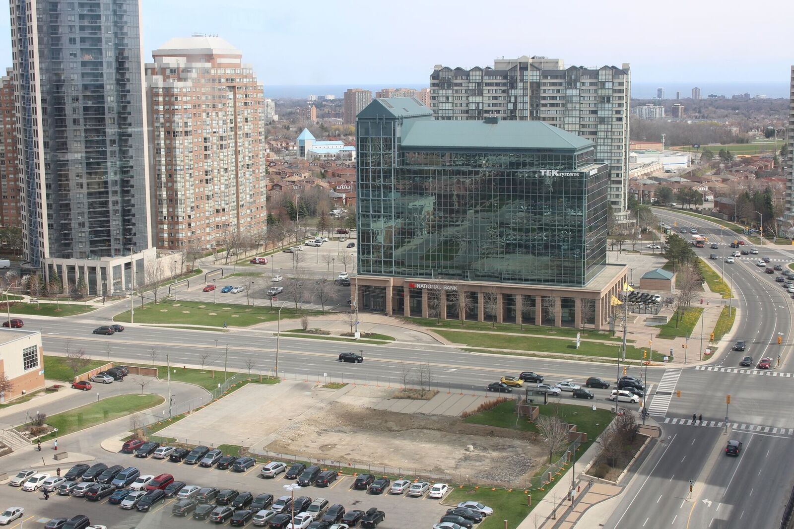 A modern building with a glass facade, surrounded by a parking lot and a busy intersection.