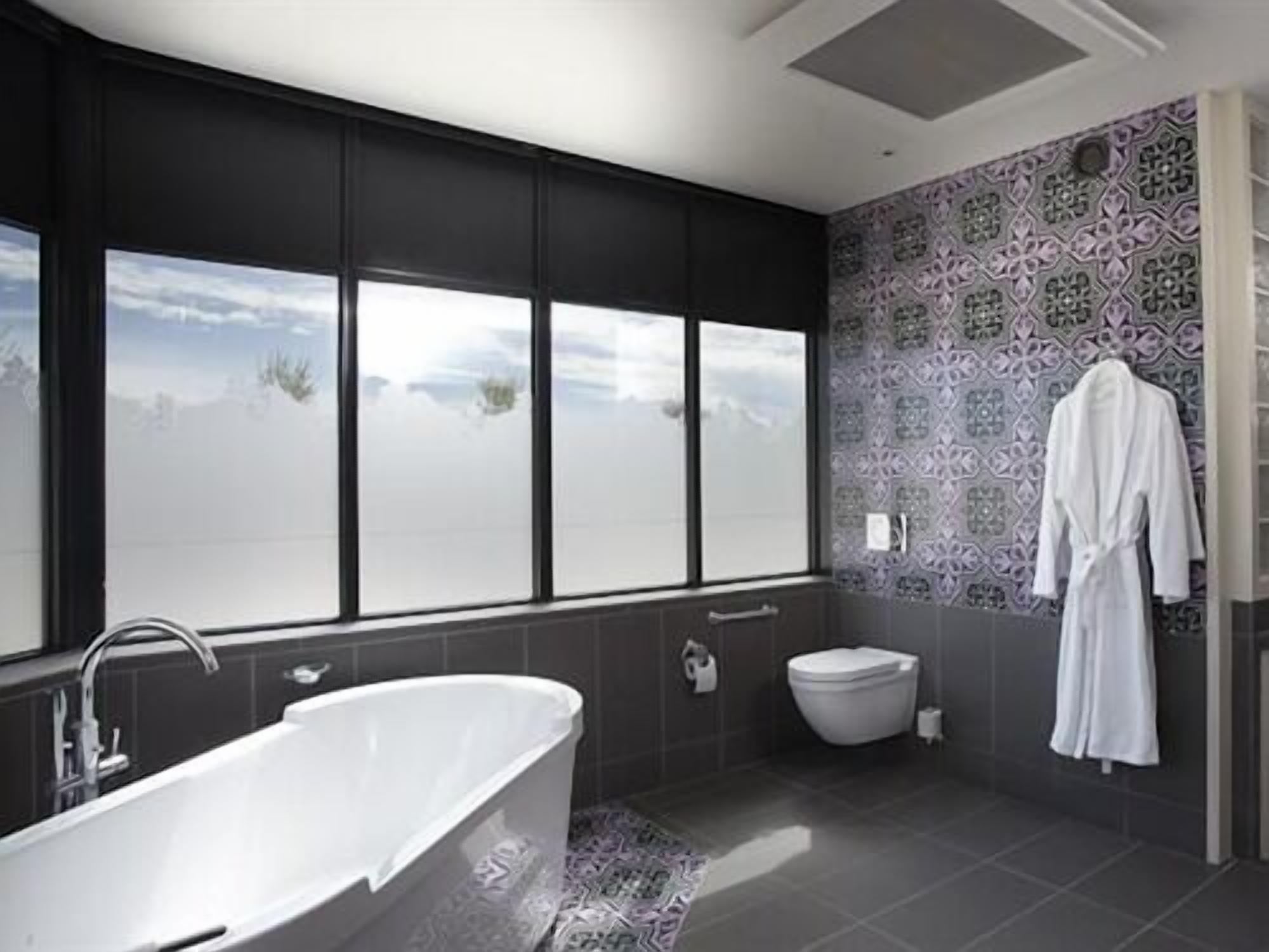 A modern bathroom with a freestanding bathtub, a toilet, and a large window offering a view of the sky.