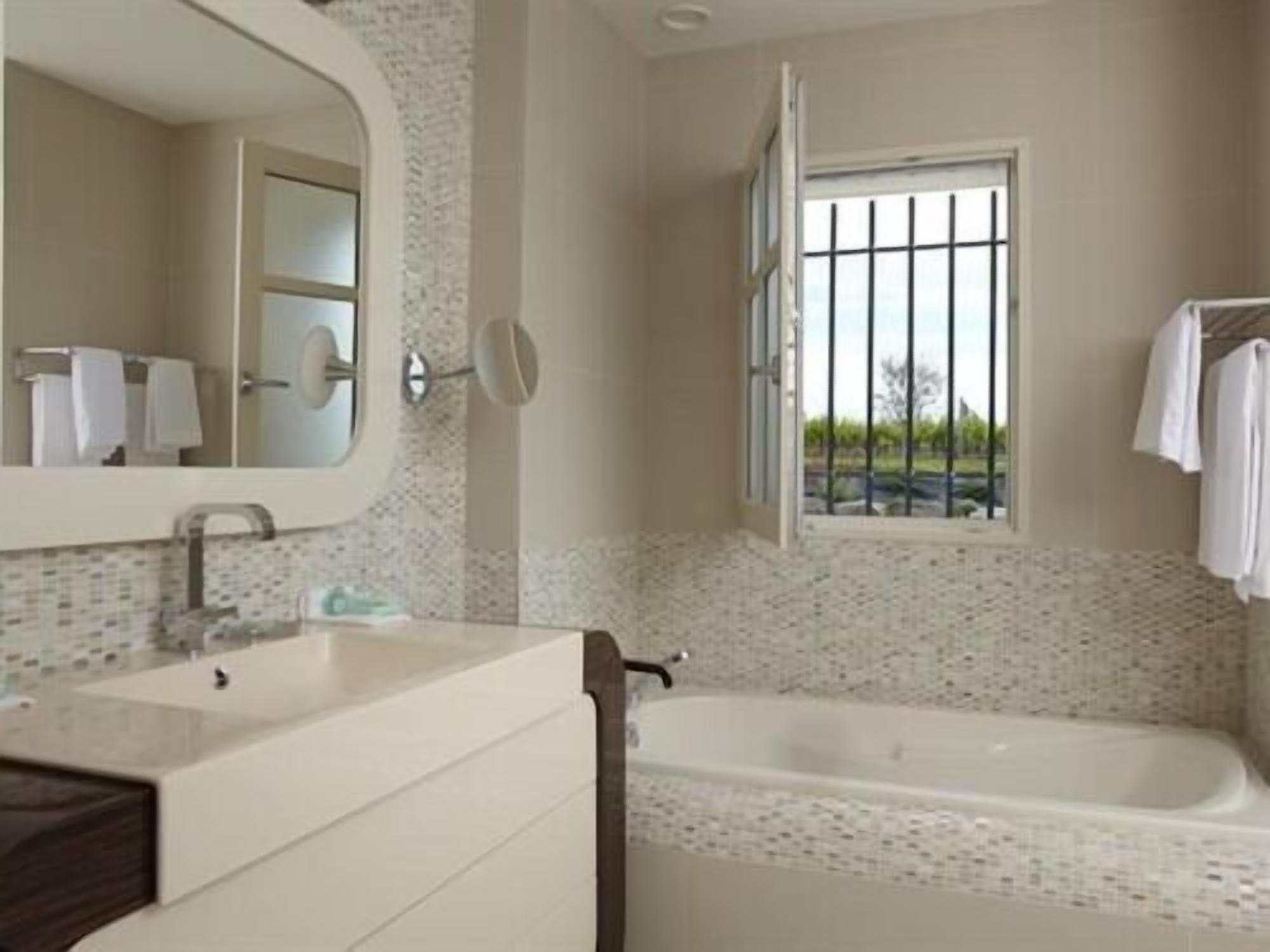 A bathroom with a large mirror, a bathtub, and a window with bars.