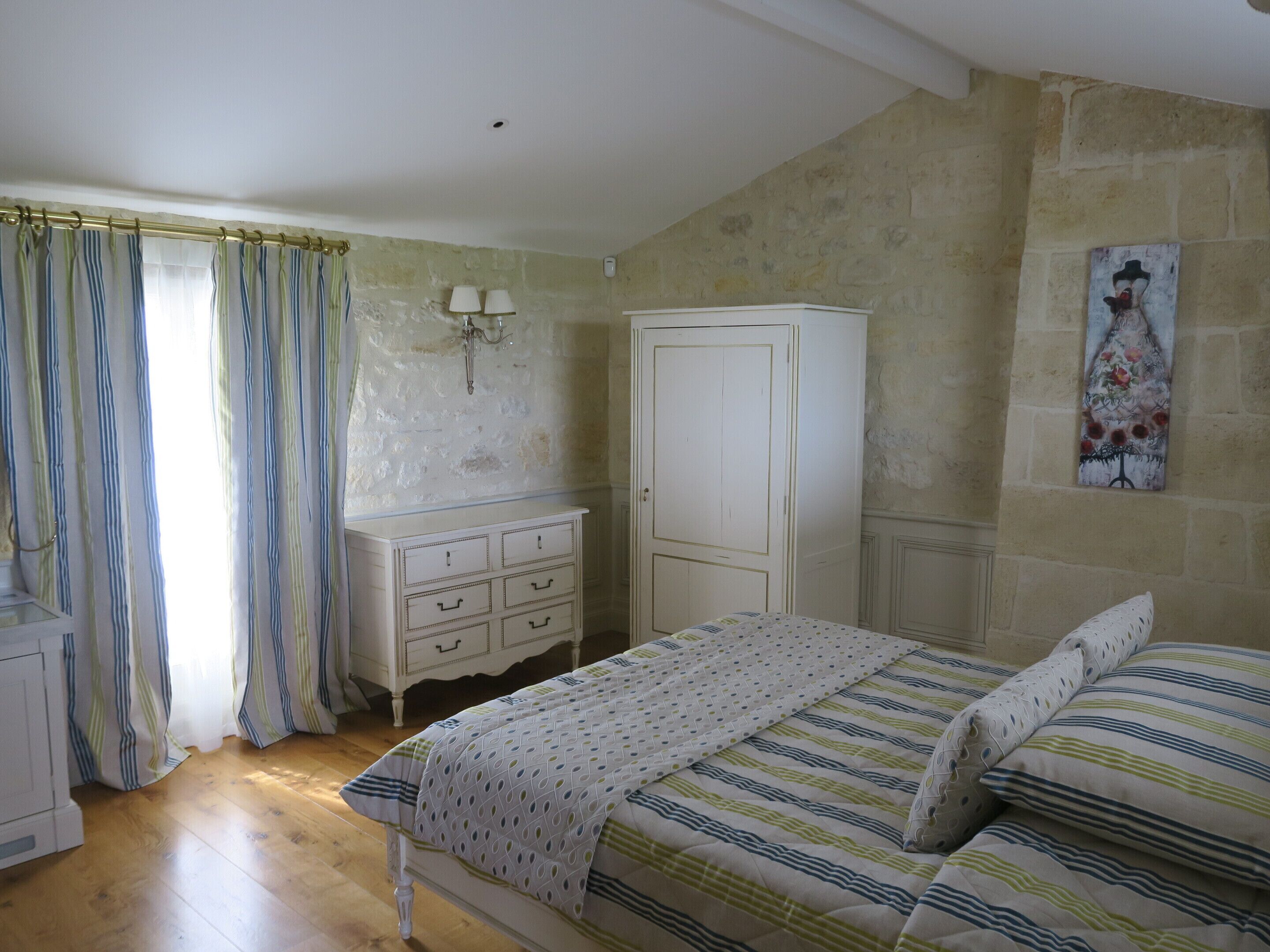 Un dormitorio con una cama de madera, un aparador blanco, un armario, un cuadro en la pared y una ventana con cortinas.