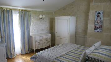 Un dormitorio con una cama de madera, un aparador blanco, un armario, un cuadro en la pared y una ventana con cortinas.