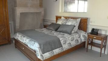 A bedroom with a wooden bed, a nightstand, a telephone, a mirror, and a stone fireplace.