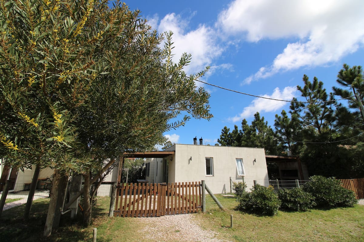 Una casa moderna con cerca de madera, un pequeño jardín y un cielo azul despejado.