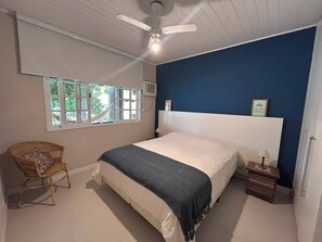 A bedroom with a bed, a ceiling fan, a window, a chair, and a bedside table. - Casa em Geribá com 2 quartos – acomoda 6 pessoas – Armação dos Búzios (Búzios)
