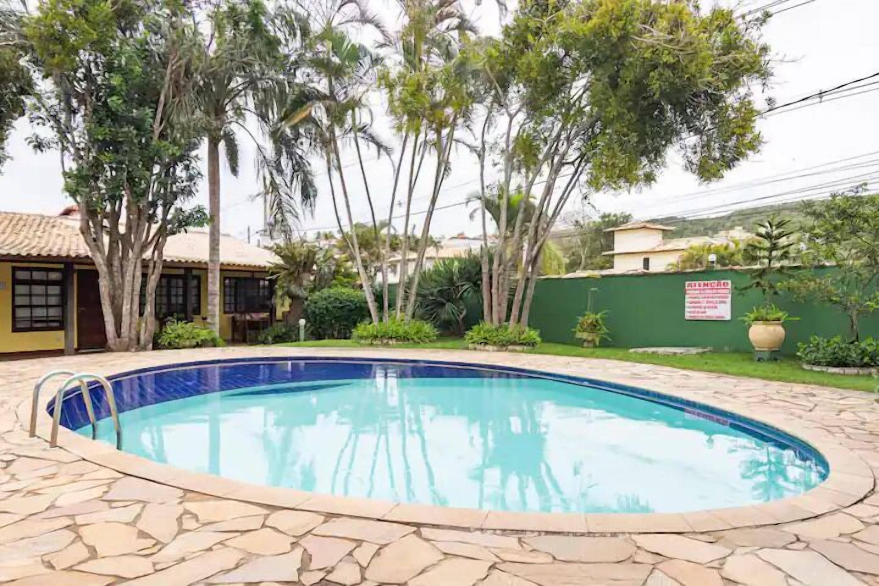 Uma piscina com borda de pedra, rodeada por árvores e um muro verde.