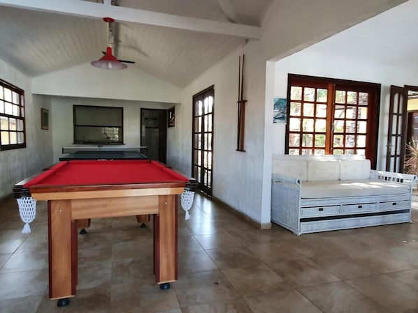 Una mesa de billar en una habitación con techos altos y ventanas amplias.