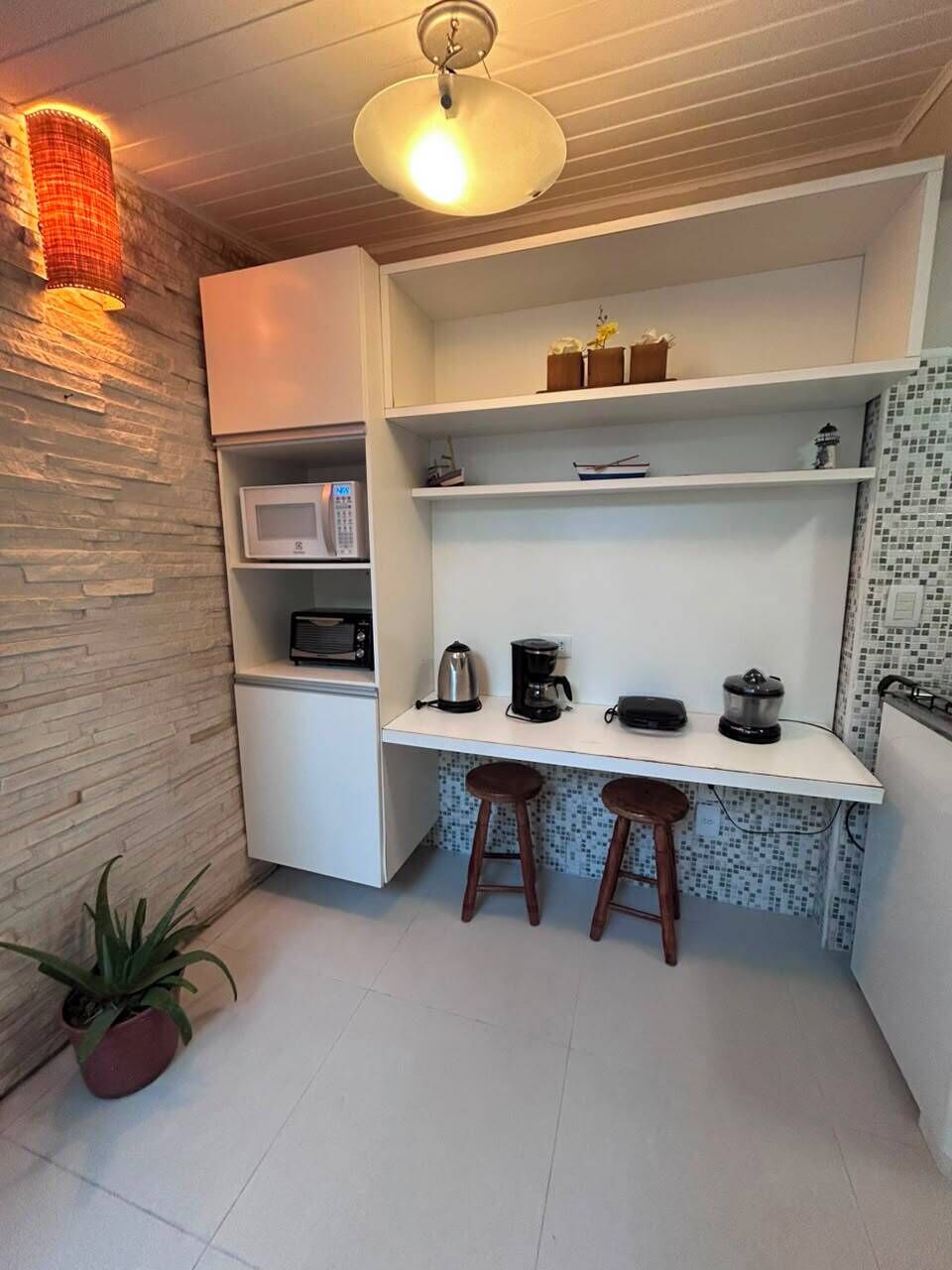 Cozinha compacta com micro-ondas, cafeteira e banquetas.