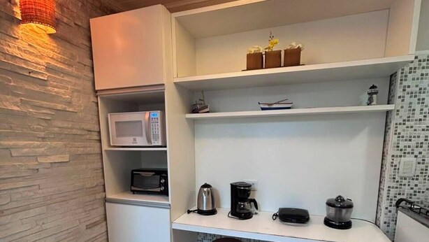 Cocina compacta con microondas, cafetera y taburetes.