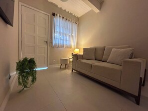 A living room with a sofa, a small table, a lamp, and a potted plant. - Casa em Geribá com 2 quartos – acomoda 6 pessoas – Armação dos Búzios (Búzios)