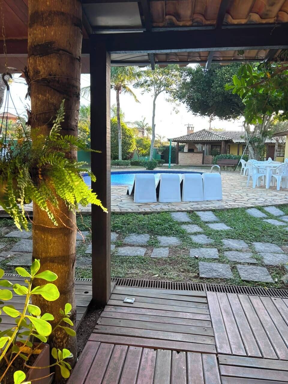 Um pátio externo com piscina, piso de pedra e cadeiras de plástico branco.