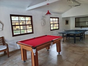 Una mesa de billar con superficie de fieltro rojo, una mesa de ping pong y una silla de madera.