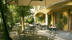 An outdoor patio area with multiple tables and chairs, surrounded by potted plants and trees. - Hotel Vanni (Misano Adriatico)