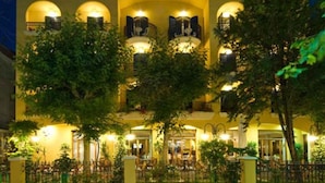 A multi-story hotel with a warm yellow facade, large windows, and a well-lit entrance. - Hotel Vanni (Misano Adriatico)