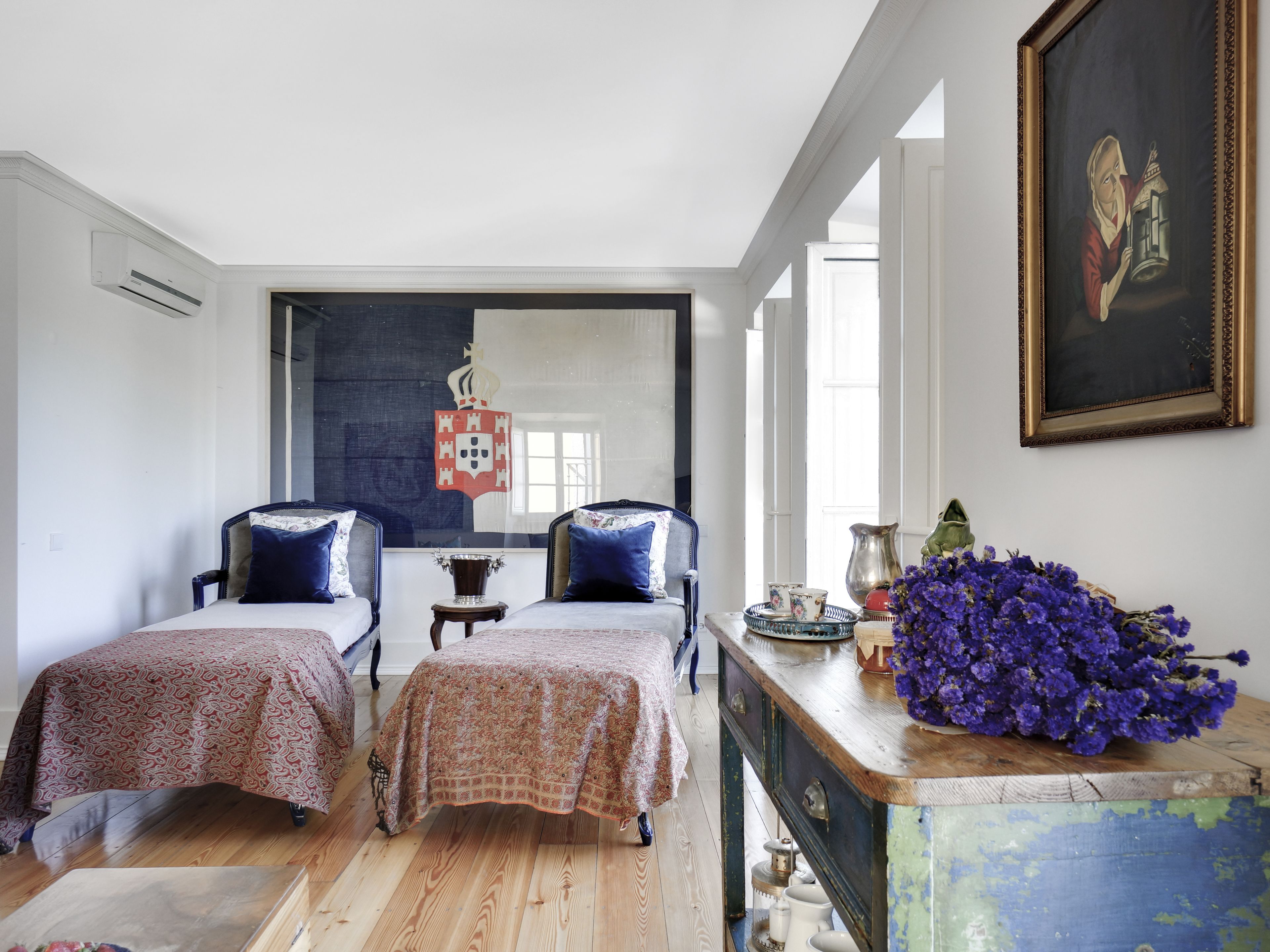 A room with two beds, a wooden dresser, a mirror, and a painting on the wall.