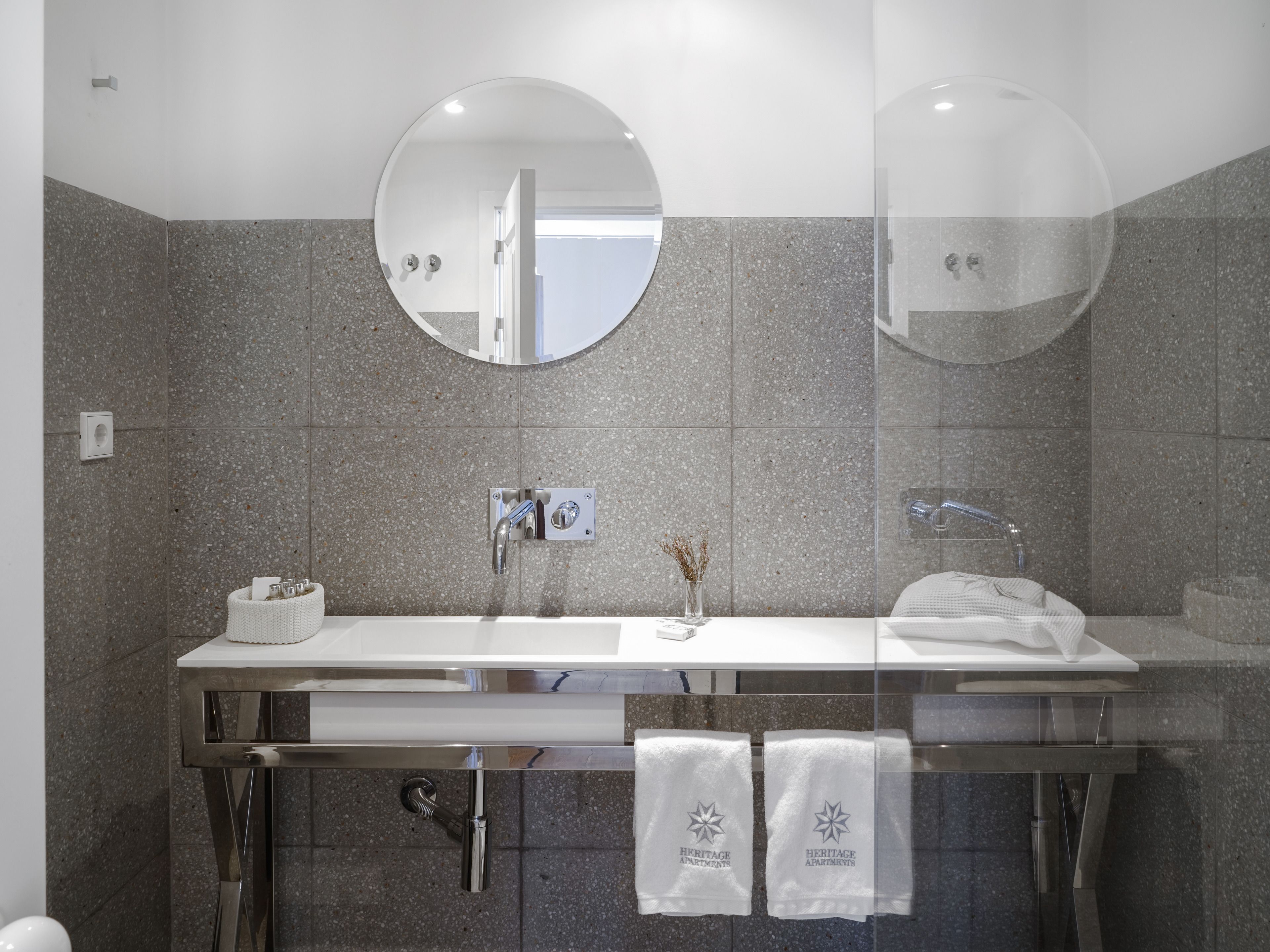 A modern bathroom with a double sink, two round mirrors, and a towel rack with towels.