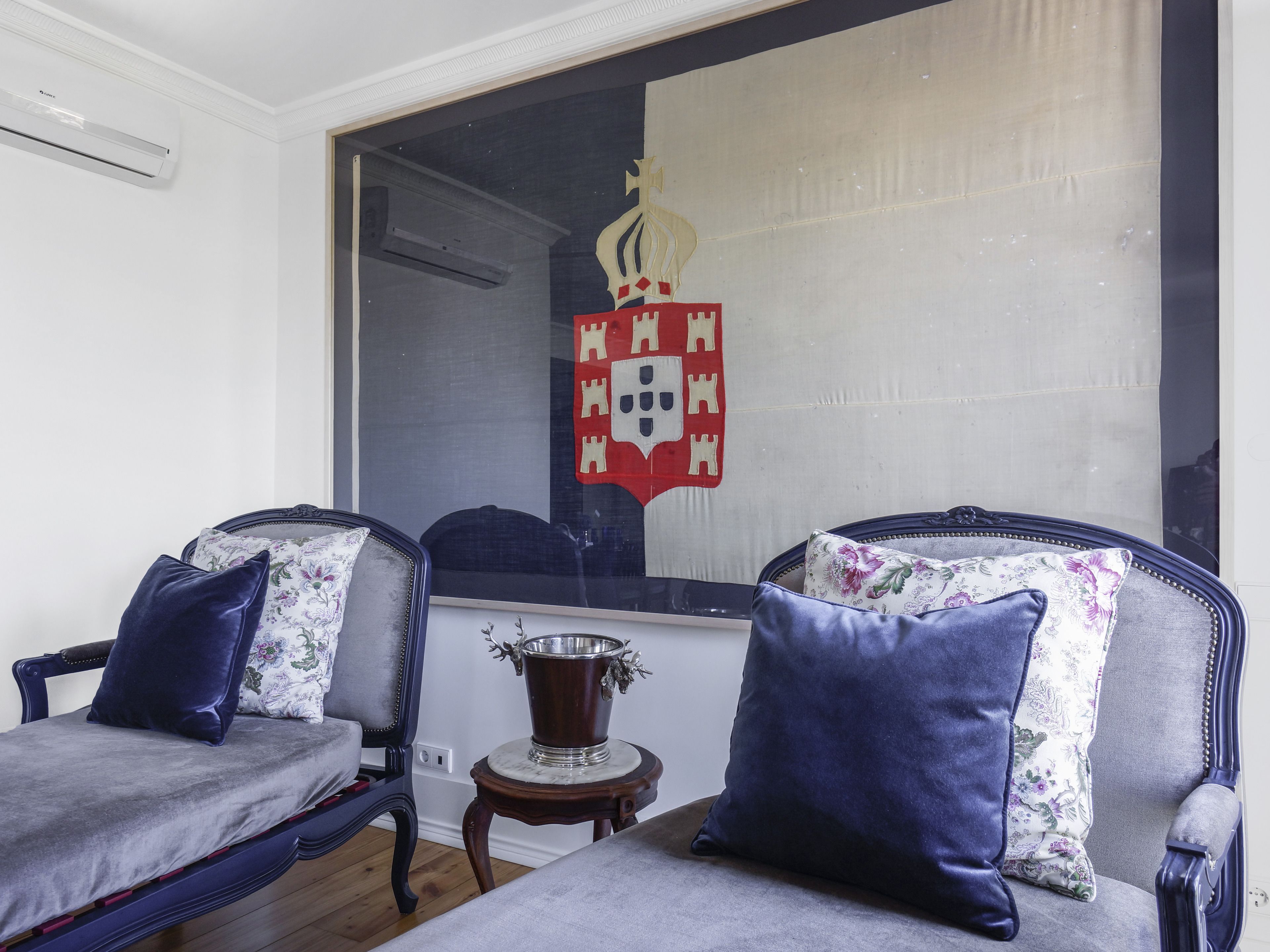 A room with two armchairs, a small table with a decorative vase, and a large window with a coat of arms.