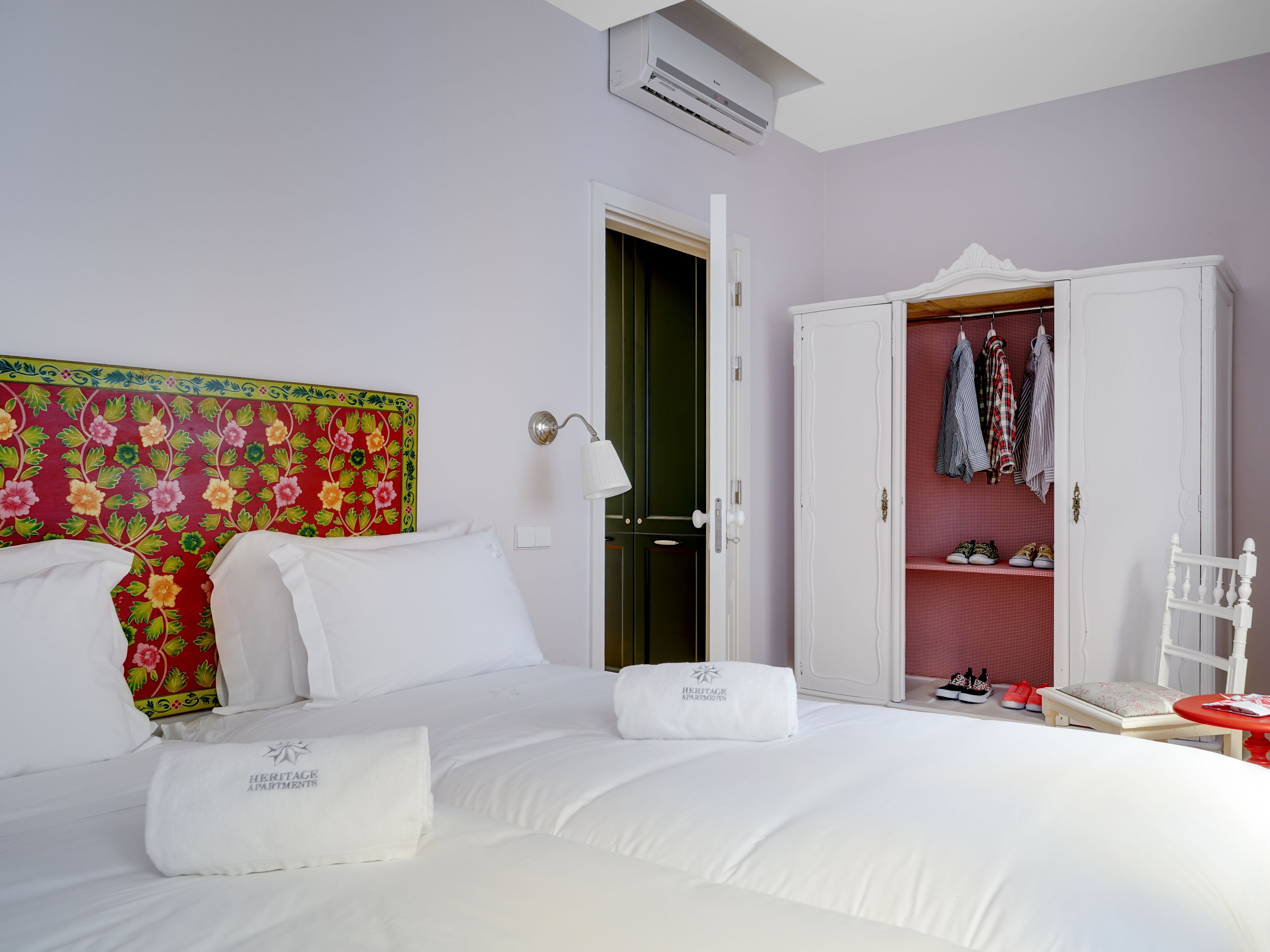 A hotel room with a large bed, a wardrobe with hanging clothes, and a door leading to a bathroom.