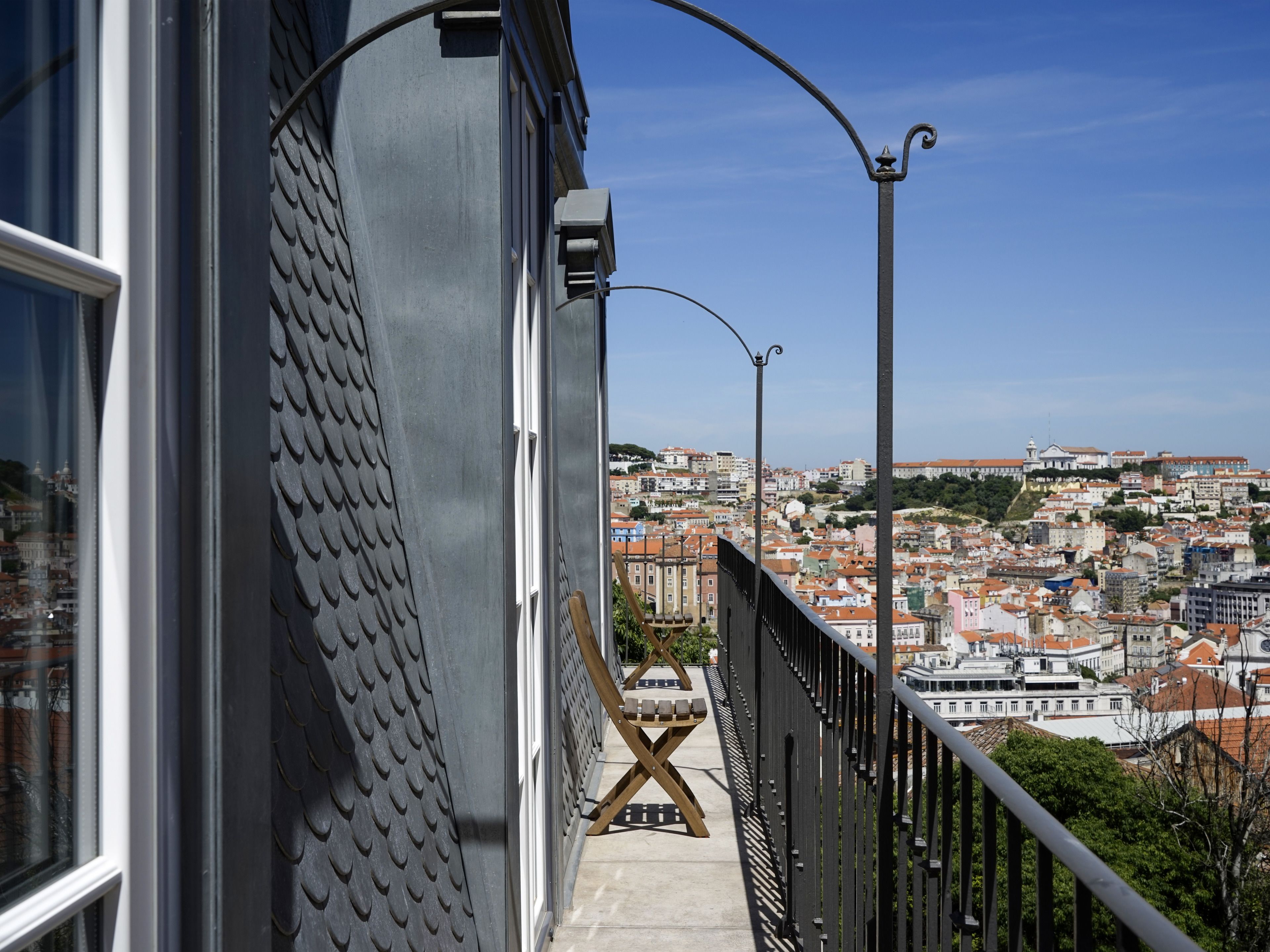 A balcony with a view of a cityscape, featuring a metal railing and a wooden X-shaped bench.