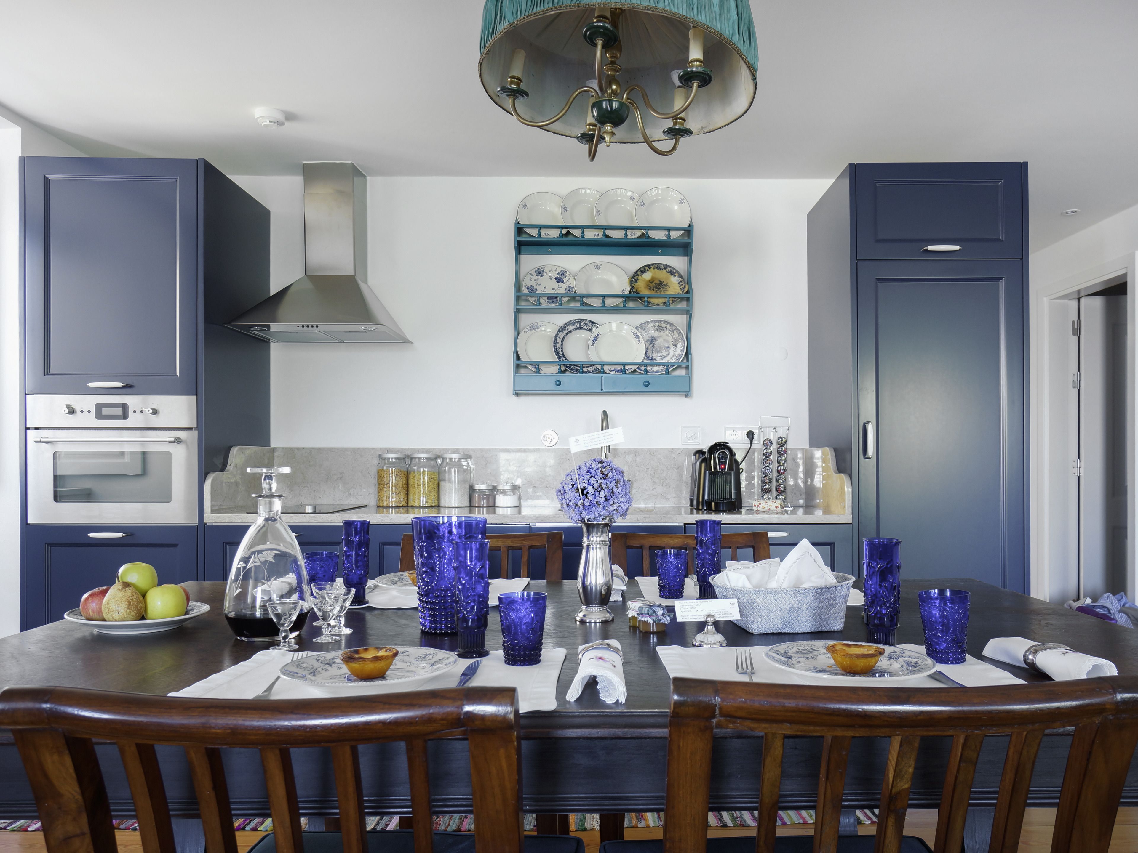 A modern kitchen with blue cabinets, a central island with blue glassware, and a decorative wall piece above the counter.
