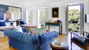 A spacious living room with a blue sofa, a wooden coffee table, and a large window offering a view of greenery.