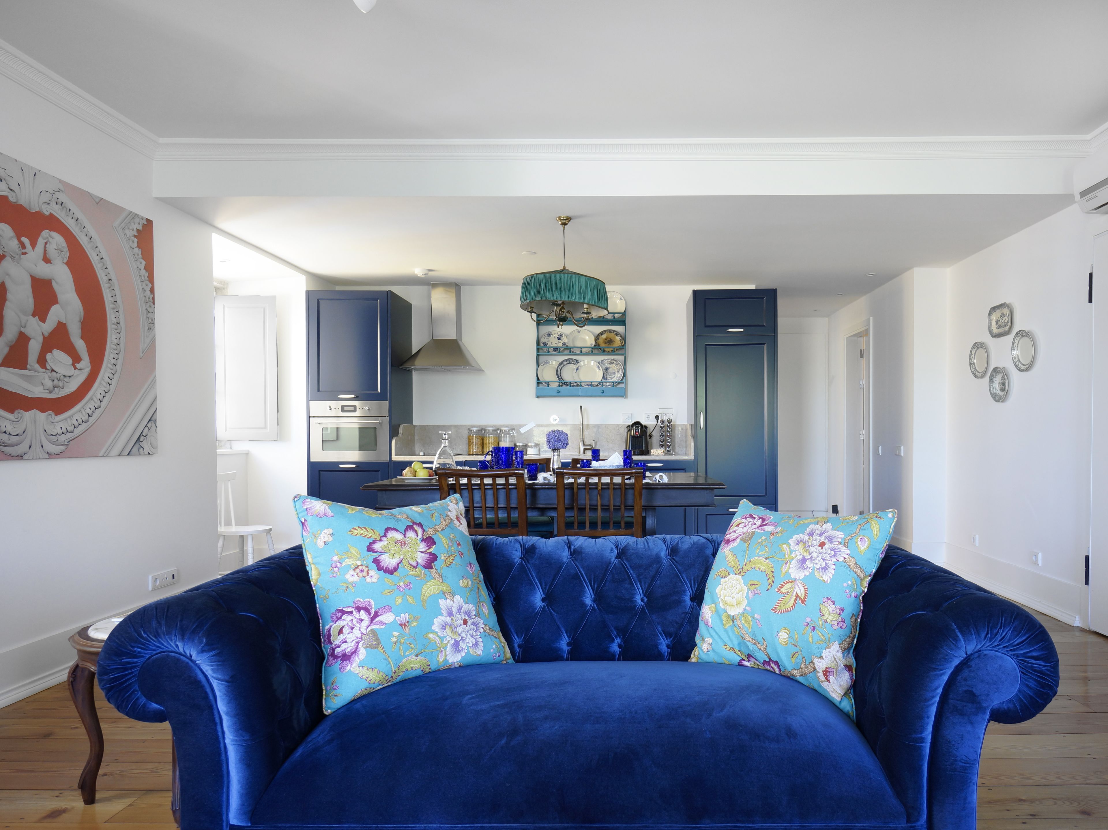 Una sala moderna con un sofá azul, una mesa de comedor y una cocina al fondo.
