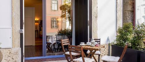 An outdoor patio with a table and chairs, a potted plant, and a sliding glass door leading to an interior space.