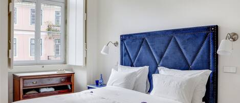 A neatly made bed with white linens, a blue upholstered headboard, and a bedside table with a lamp.