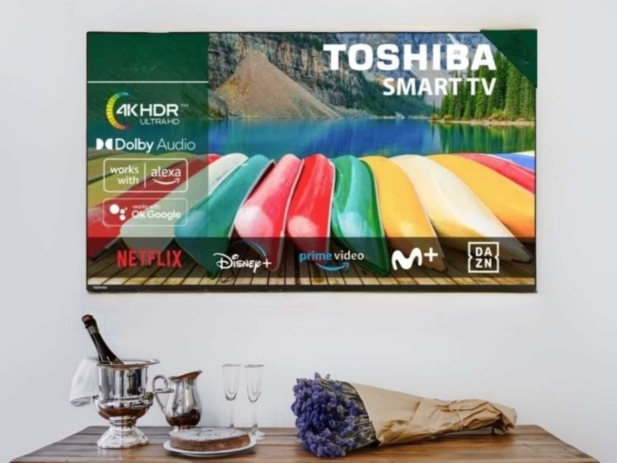 A wall-mounted TV with a Toshiba SmartTV logo, 4K HDR, Dolby Audio, and logos for Netflix, Disney+, Prime Video, M+, DAZN, and Alexa compatibility.