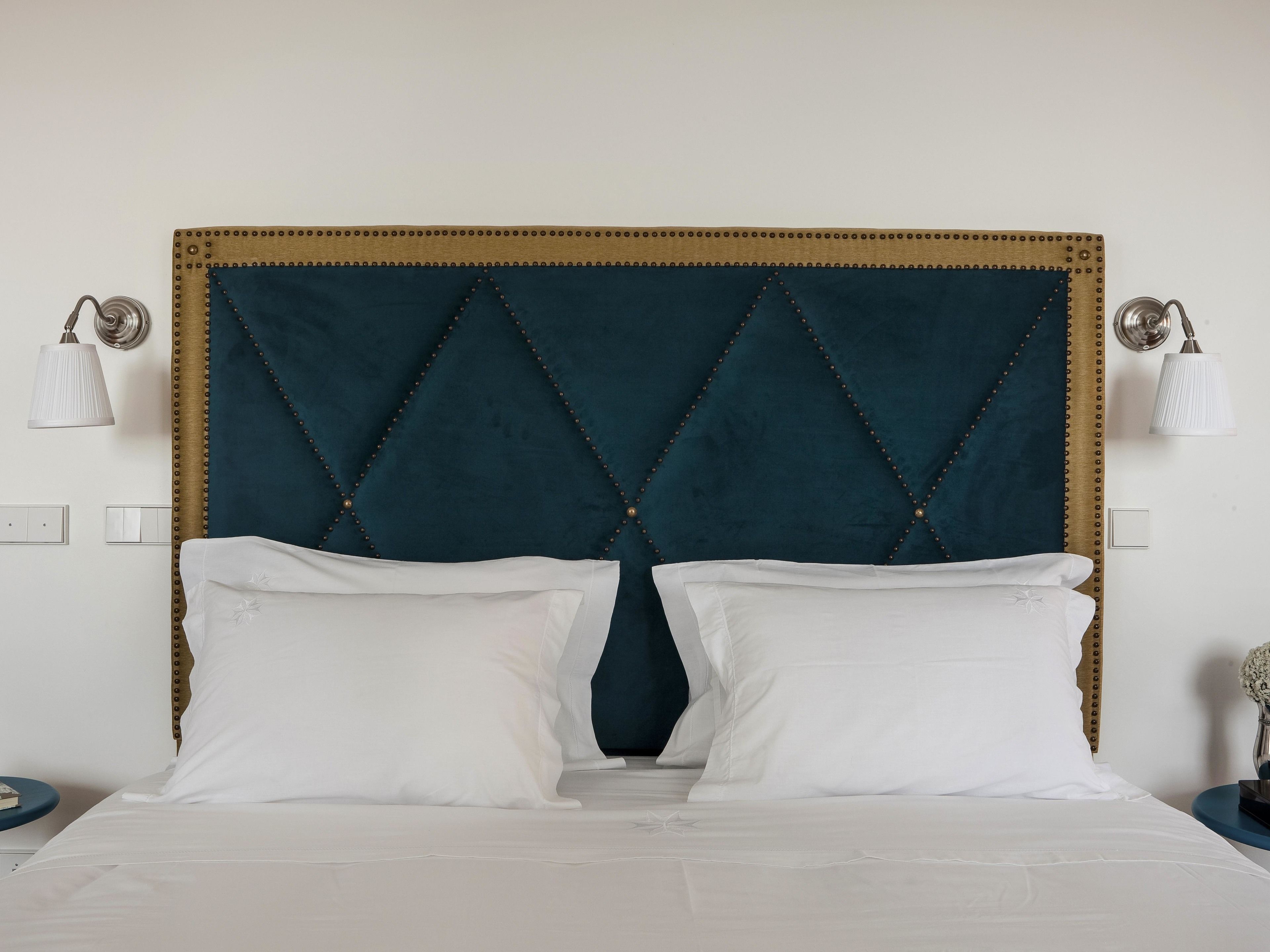 A bed with a dark blue upholstered headboard, white pillows, and a white bedspread.