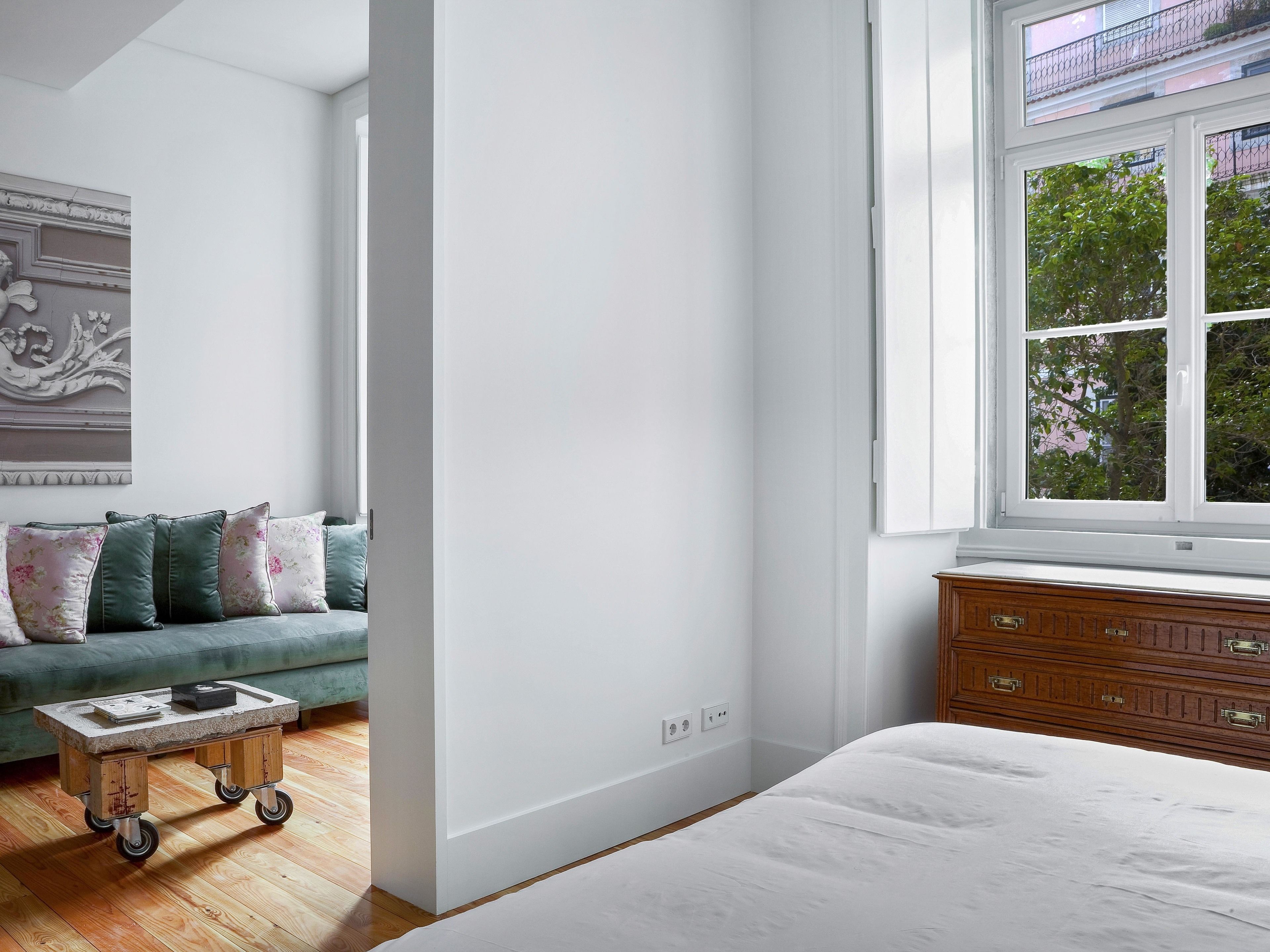 A bedroom with a large bed, a wooden dresser, a green sofa, and a small table with wheels.