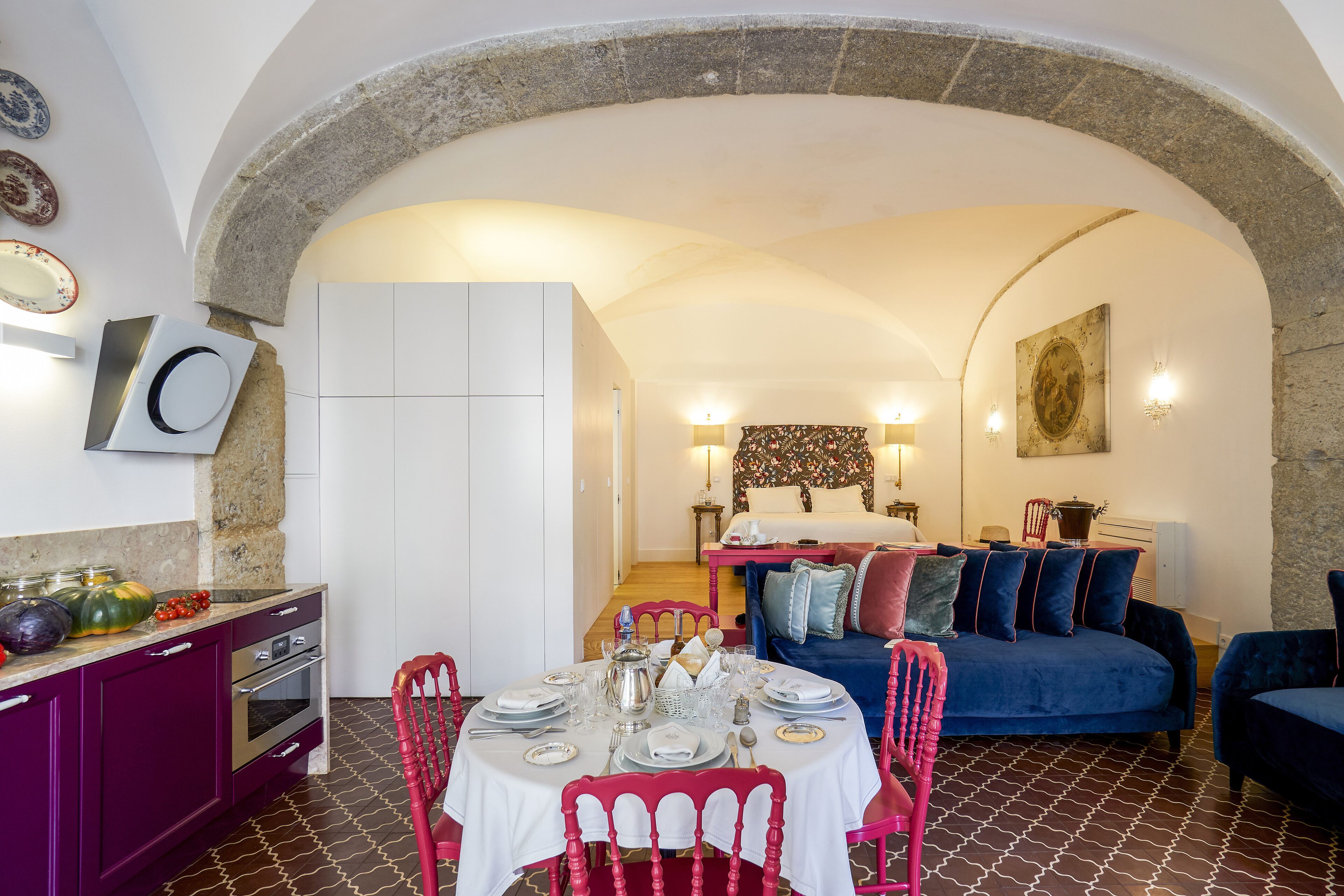 A dining area with a table set for four, a kitchen with purple cabinets, and a living area with a blue sofa and decorative pillows.