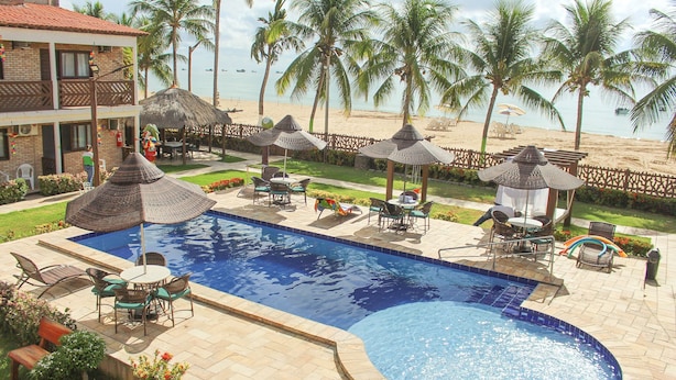 Une piscine avec des chaises longues et des parasols, une vue sur la plage et des palmiers.